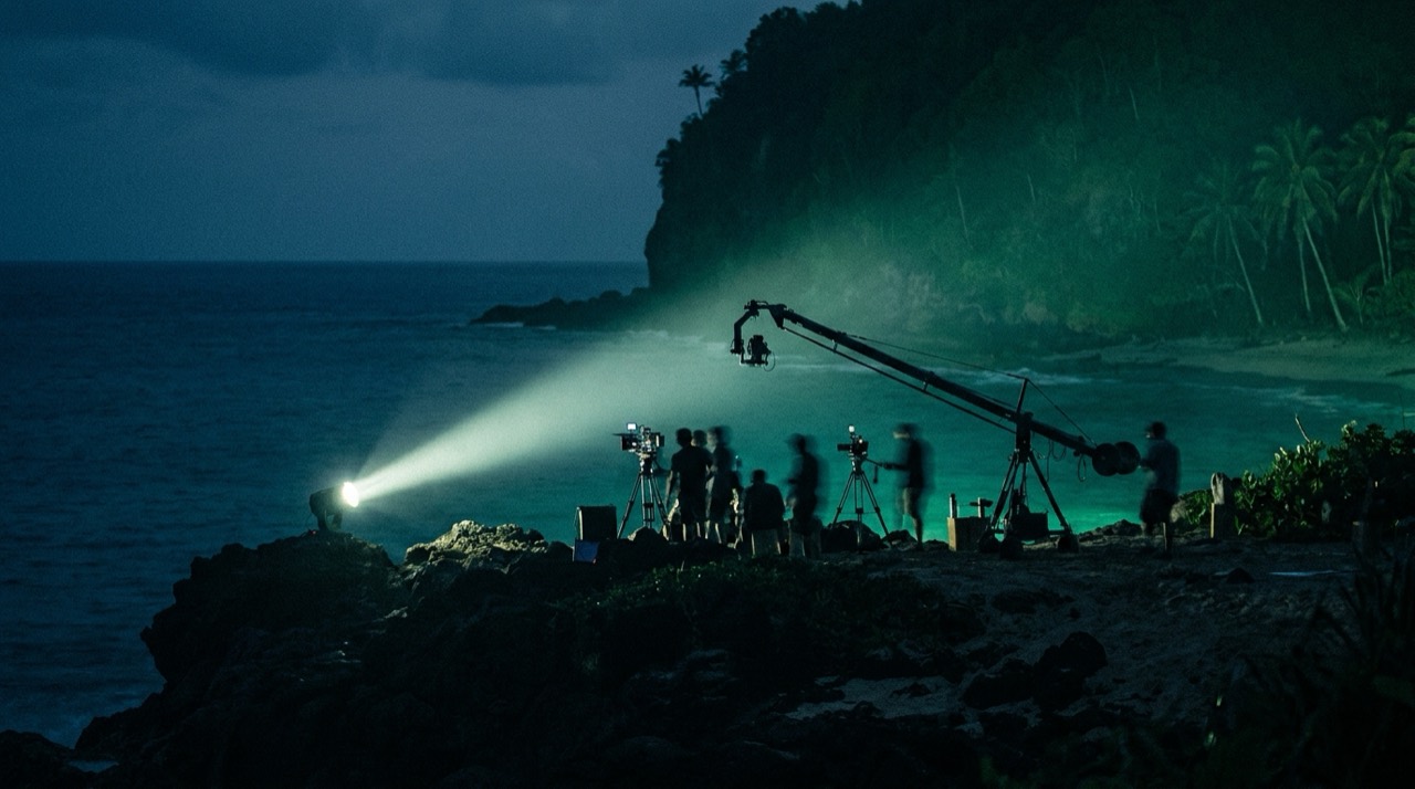 Photo : île tropicale au crépuscule, projecteur de télé-réalité et rig de tournage, ambiance bleu-vert